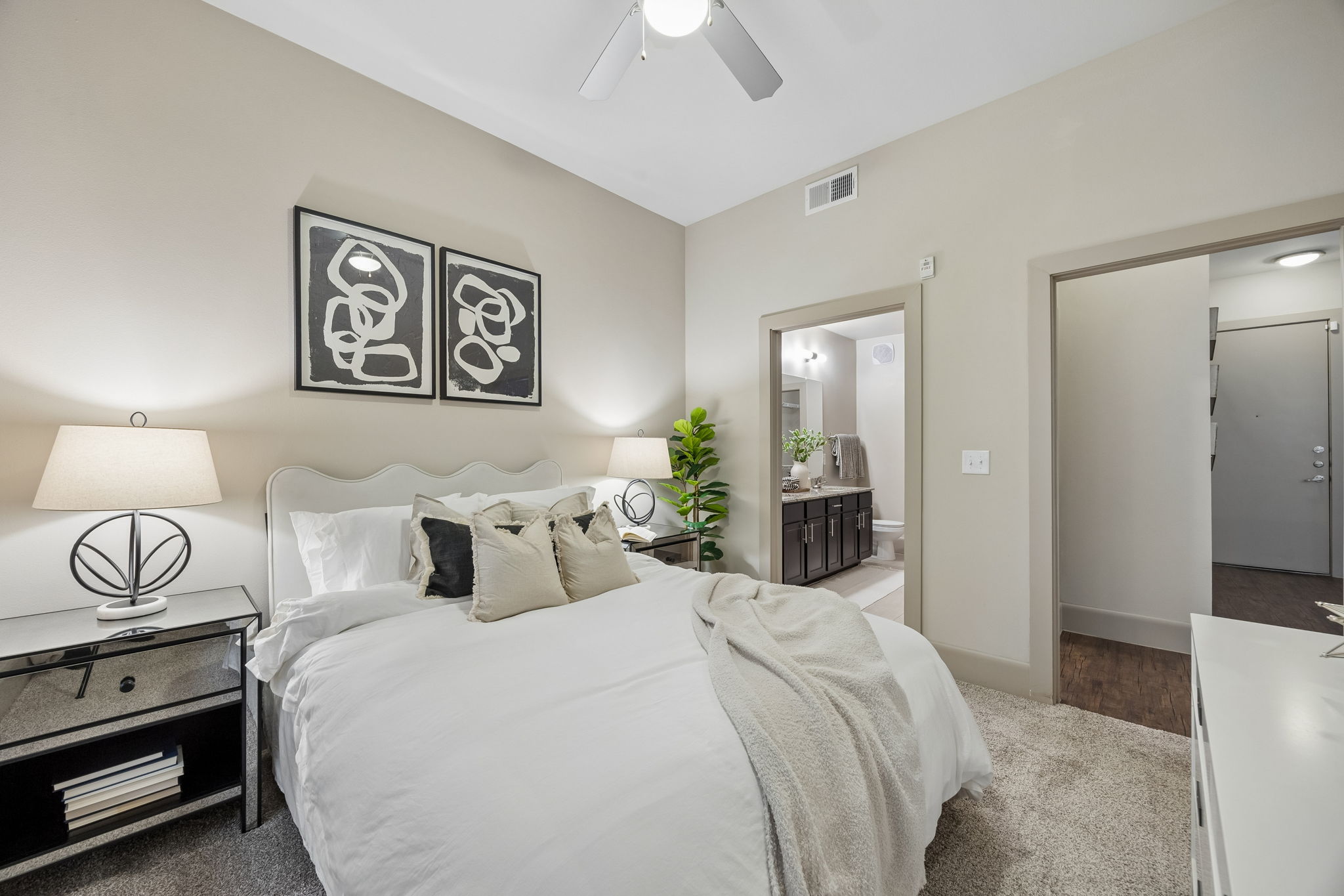 An interior view of a bedroom with bathroom in the background and 2 night stands.