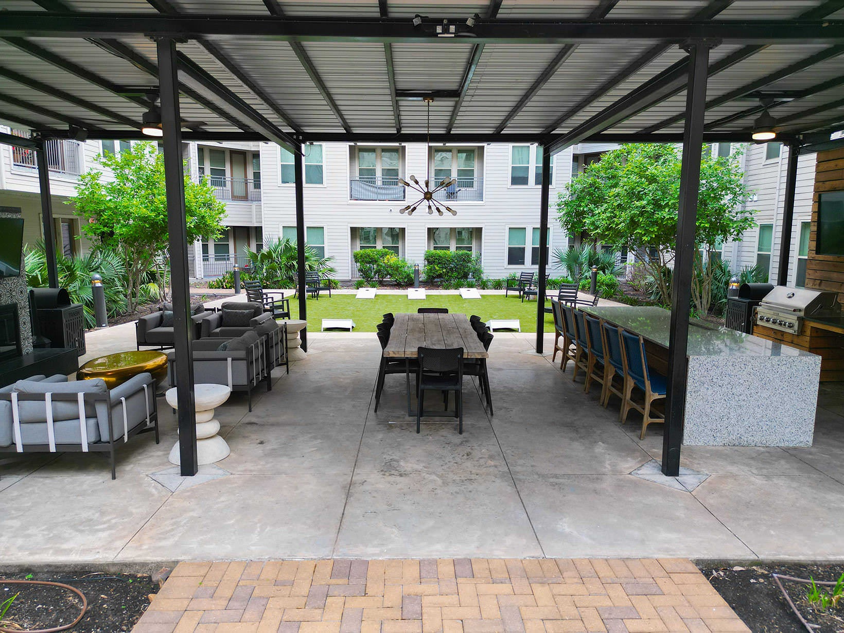 Covered Patio tables, chairs, grills and fireplace next to game lawn